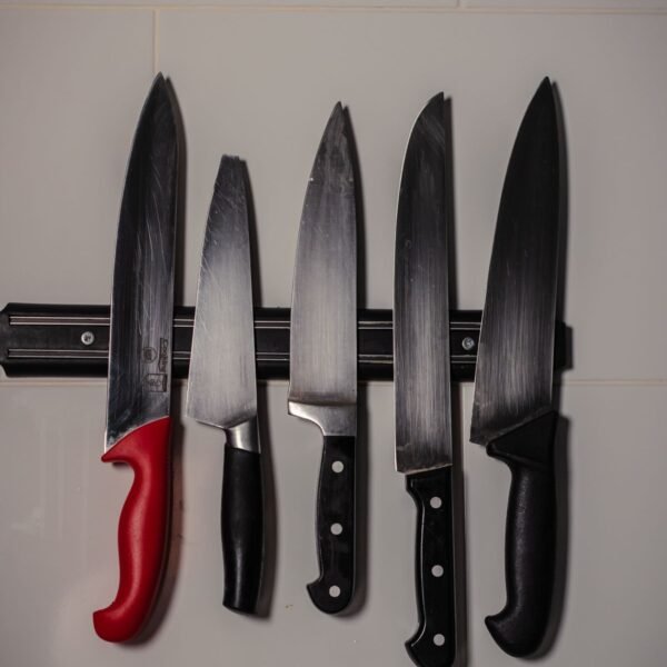Five stainless steel kitchen knives on a white tiled wall