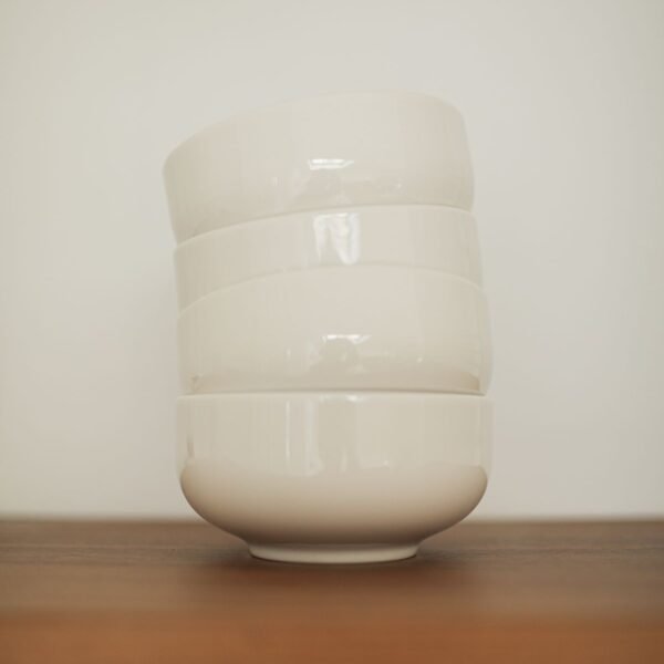 Stack of four white ceramic bowls on a light background